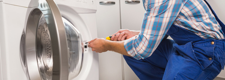 A handyman in blue overalls repairing a dryer.